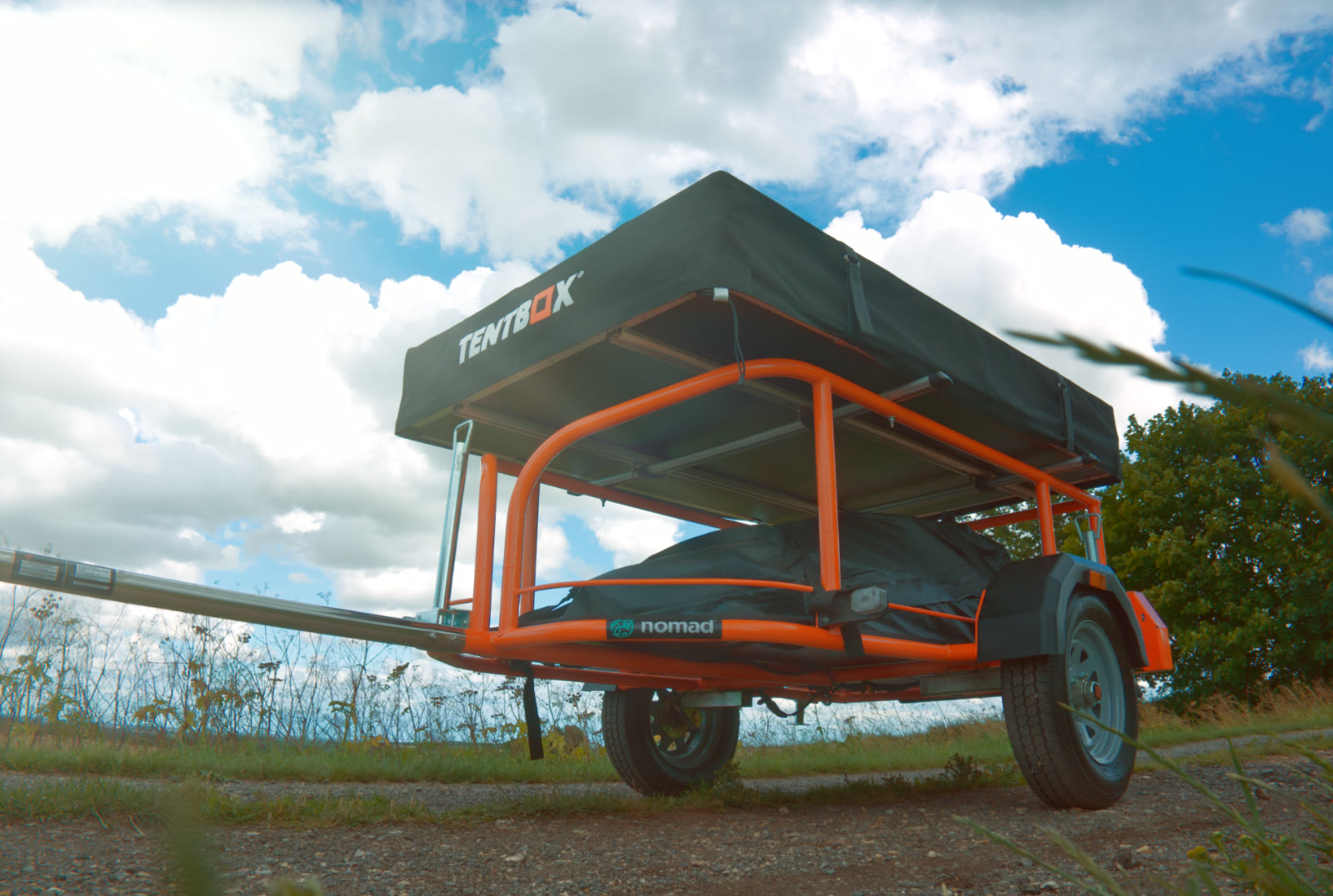 Orange Nomad adventure trailer fitted with a TentBox beneath a blue sky